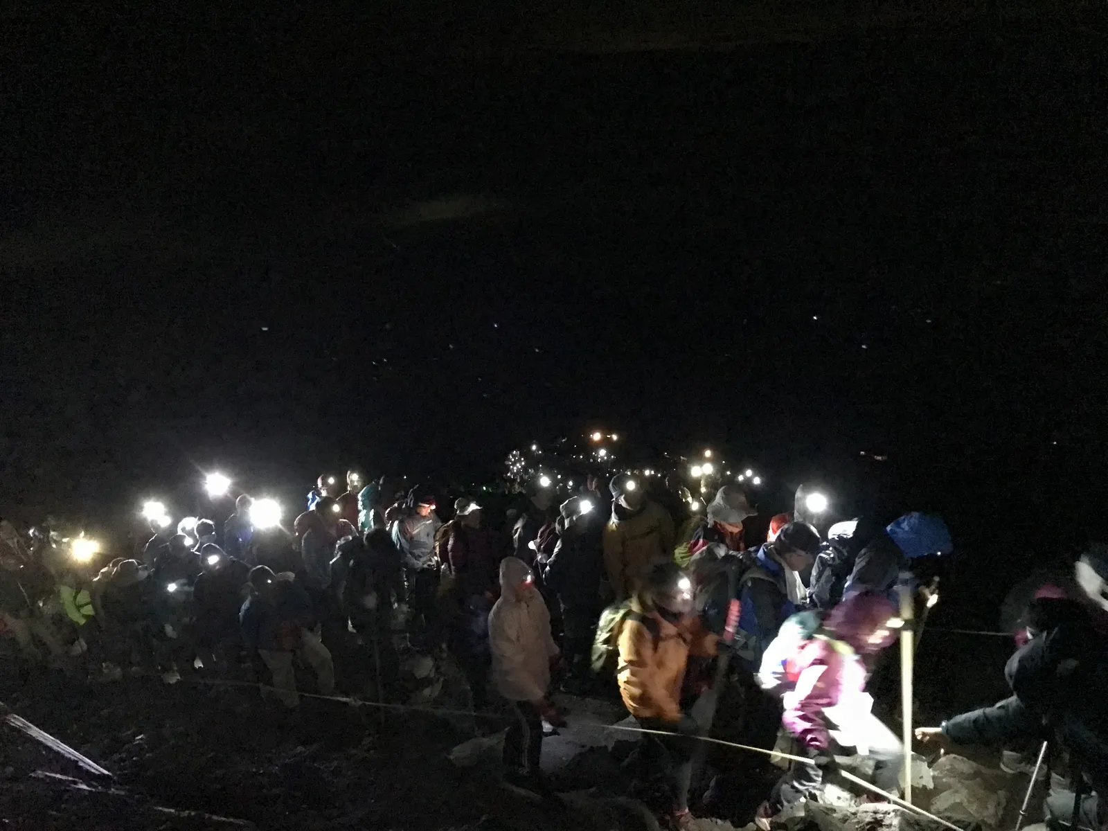 富士山で未明にご来光を目指す登山者の列が、それぞれのヘッドライトを点けて山頂直下の暗い登山道を進んでいる様子