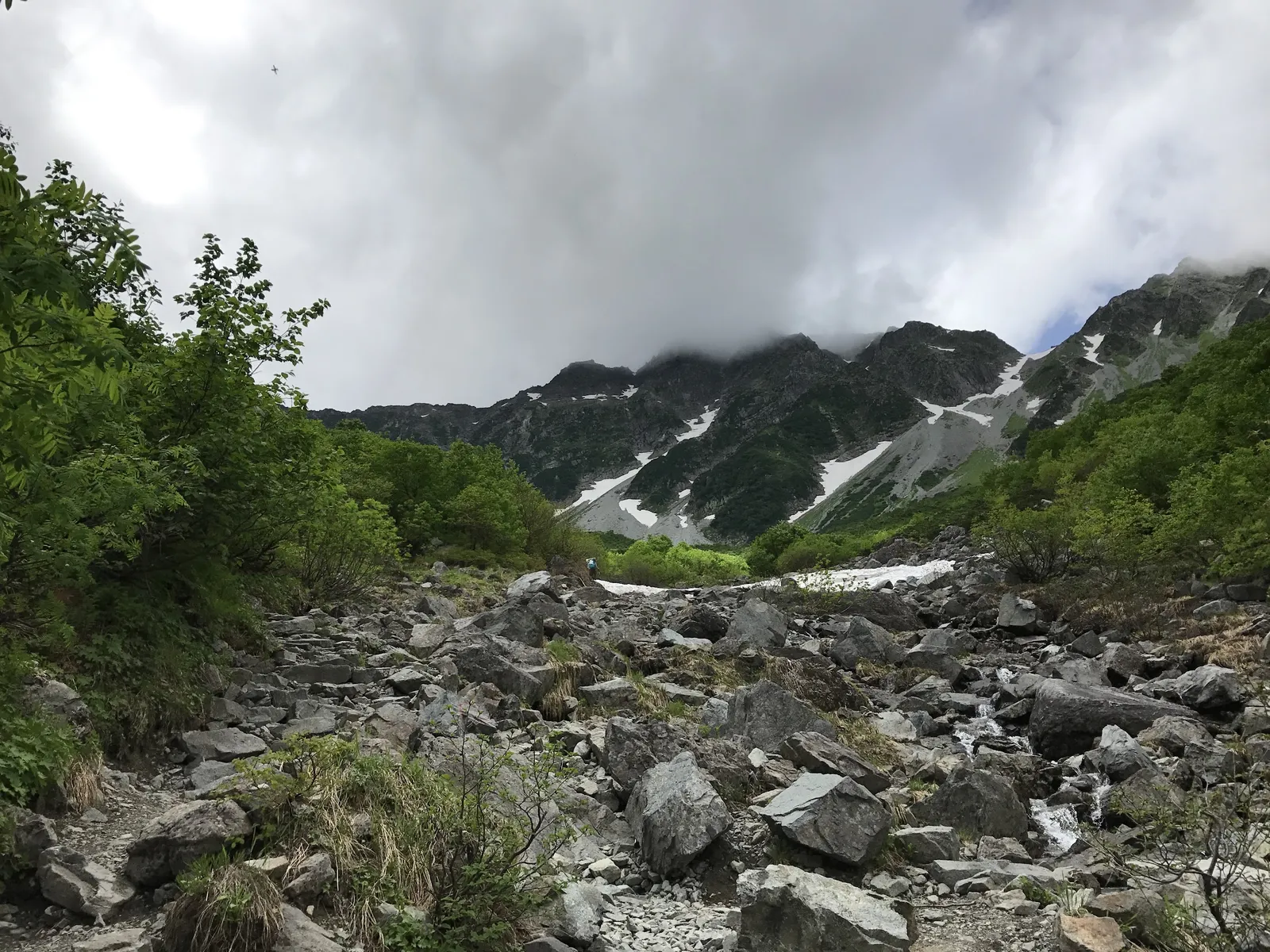 涸沢手前のガレた岩の登山道と、霧がかった谷に残る雪渓