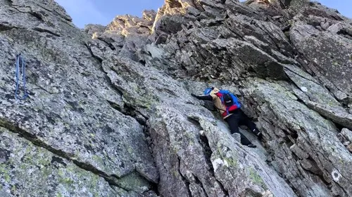 垂直に近い岩壁に張り付くように手足を掛けてよじ登る登山者。ロープなどの補助器具は見当たらない