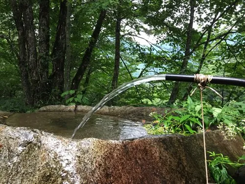 登山道の水場で石鉢にホースから清水が注がれている様子