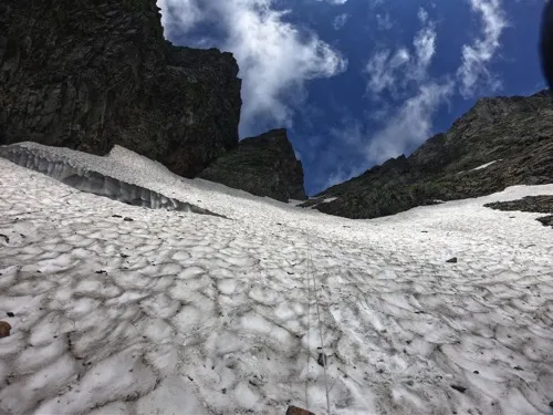 急な角度で切れ込んだ雪渓の谷を見上げた写真。雪面に沿ってロープが張られている