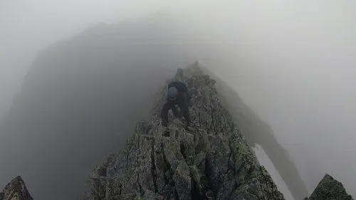 両側が切れ落ちた細い岩の刃の上を、またぐような姿勢で慎重に下る登山者の後ろ姿