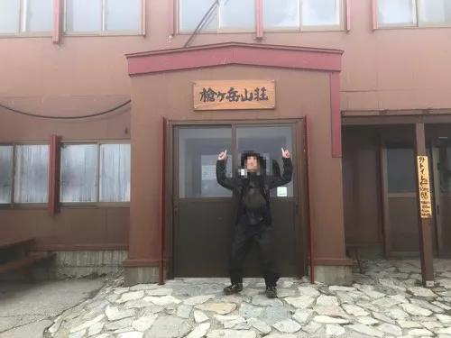 霧に包まれた槍ヶ岳山荘の玄関前でポーズする登山者