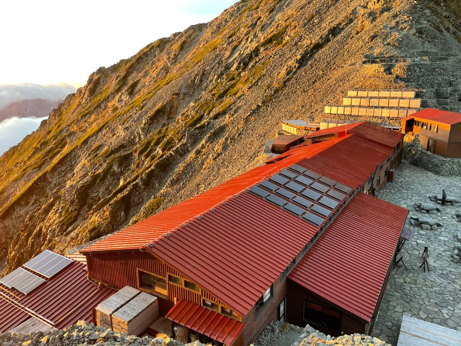 夕日に染まる穂高岳山荘の赤い屋根の建物群と、石積みのテント場を上から見下ろした様子
