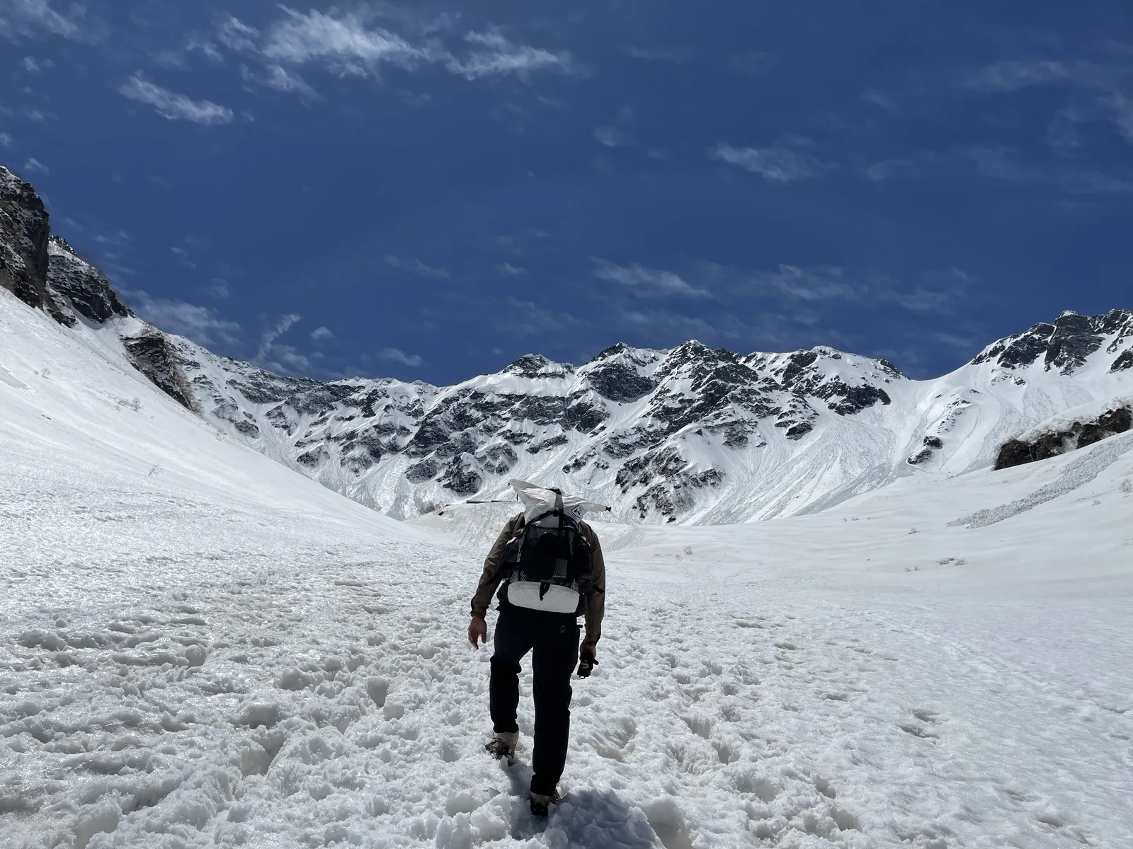 残雪期の涸沢で、雪に覆われた斜面についた無数の踏み跡を登る登山者の後ろ姿