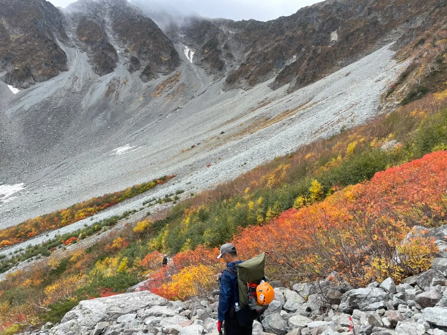 紅葉の涸沢でザックにオレンジのヘルメットを外付けして歩く登山者