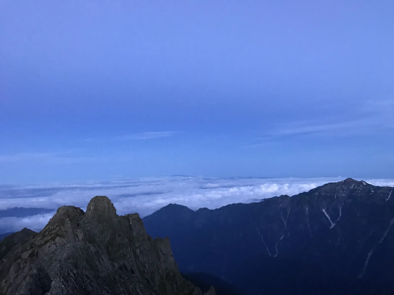 夜明け前の濃紺の空に浮かぶ山の稜線のシルエットと雲海。気温が大きく下がる未明の登山シーンの実写