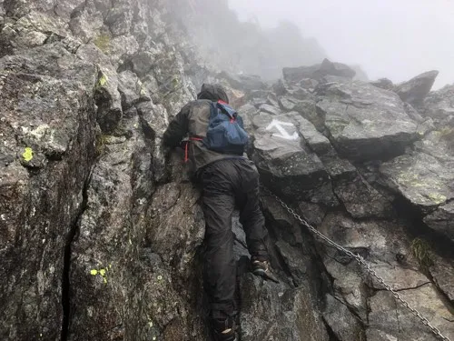 霧の中、槍ヶ岳の穂先で鎖沿いに岩場を登る登山者の実際の様子