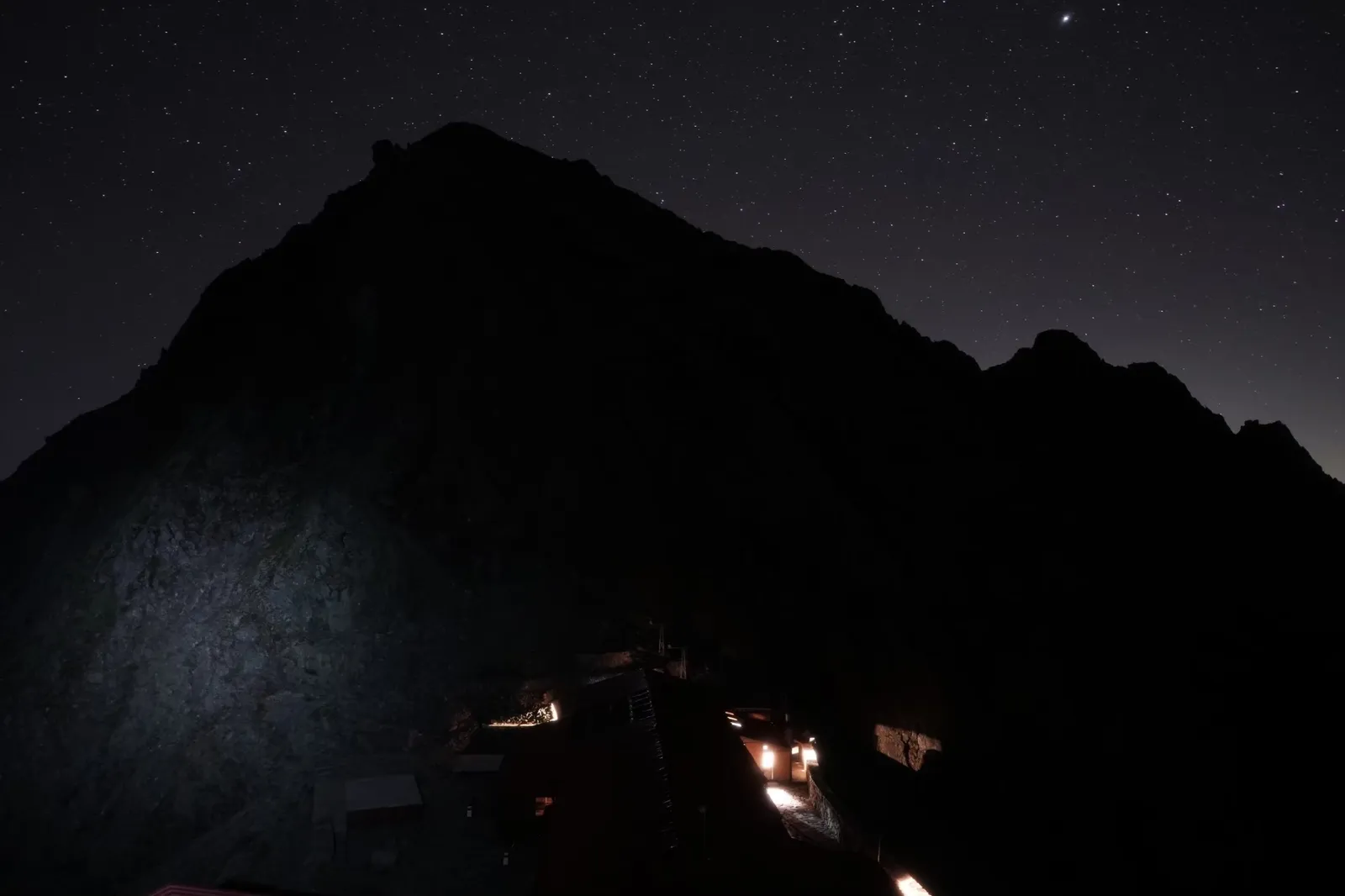 夜の黒い岩峰の下に山小屋の明かりが灯る穂高岳山荘